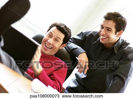Man sitting with feet on desk using laptop, second man looking over his shoulder View Large Photo Image Stock Image - Man sitting with feet on desk using laptop, second man looking over his shoulder. Fotosearch