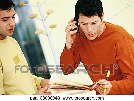 Men looking at newspaper, one using cell phone View Large Photo Image Stock Photo - Men looking at newspaper, one using cell phone. Fotosearch
