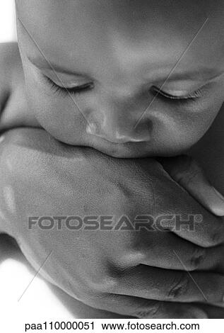 Stock Image - Baby held in adult's hand, close-up, b&w. Fotosearch