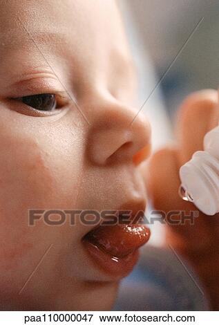 Stock Photo - Baby's face and end of vitamin dropper, close-up. Fotosearch