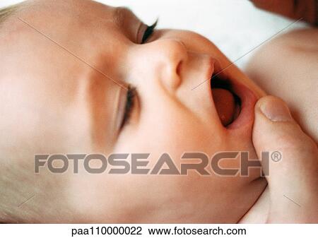 Stock Image - Baby's face with adult finger on chin, close-up. Fotosearch