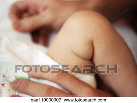 Stock Photo - Baby's leg and adult hand on baby's diaper, close-up. Fotosearch
