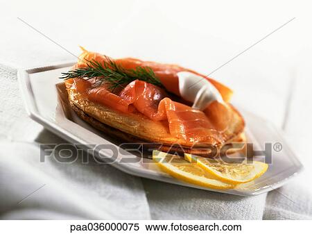 Stock Photography - Blinis topped with smoked salmon, herbs and fresh cream, with lemon slices, on plate. Fotosearch