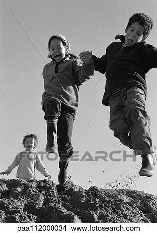 Picture - Boy and girl jumping, second girl in background, low angle view, b&w. Fotosearch