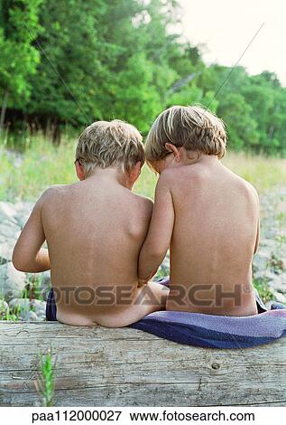 Stock Photo - Boy and girl sitting on towel, outside, rear view. Fotosearch