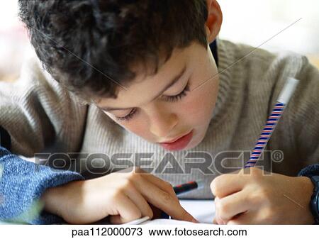 Stock Image - Boy bending head over notebook, writing, close-up. Fotosearch