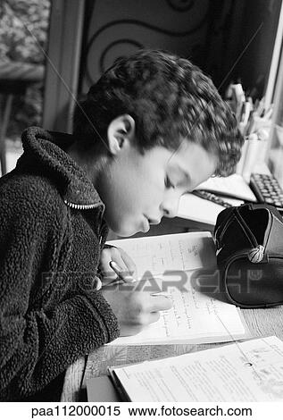 Stock Photography - Boy sitting at desk, writing in notebook, side view, b&w. Fotosearch