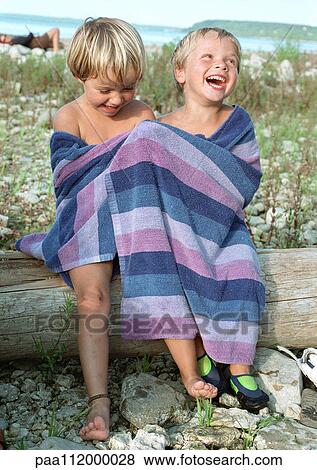 Stock Photo - Girl and boy in bath towel sitting on log, smiling. Fotosearch