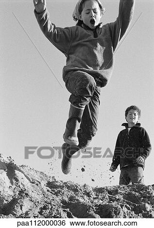 Stock Photograph - Girl jumping, boy in background, low angle view, b&w. Fotosearch