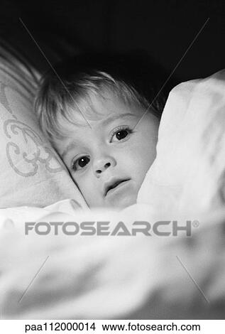 Picture - Little girl in bed under blanket, close-up, b&w. Fotosearch