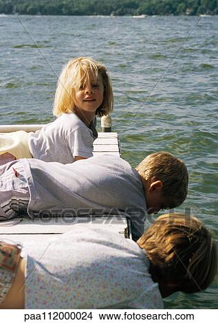 Picture - Two girls and boy lying on a wooden dock. Fotosearch