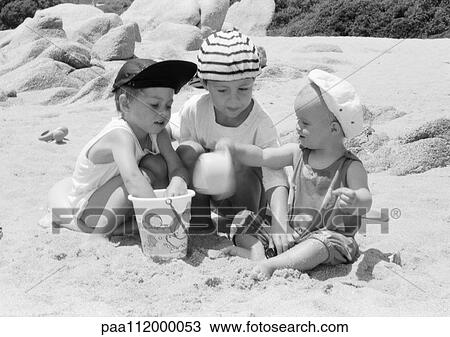 Stock Image - Two girls and boy playing in sand. Fotosearch