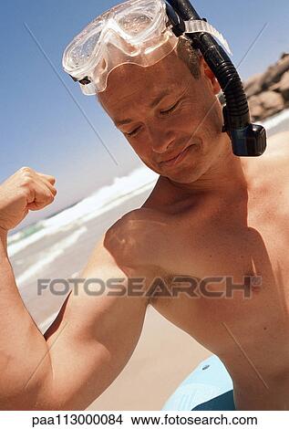 Picture - Close-up of man flexing with mask and snorkel on head at the beach.. Fotosearch