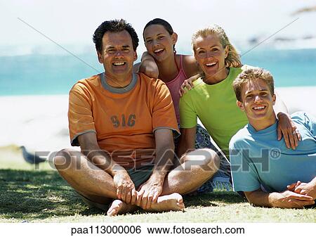 Stock Photograph - Family sitting on beach, smiling, front view, sea in background, portrait.. Fotosearch