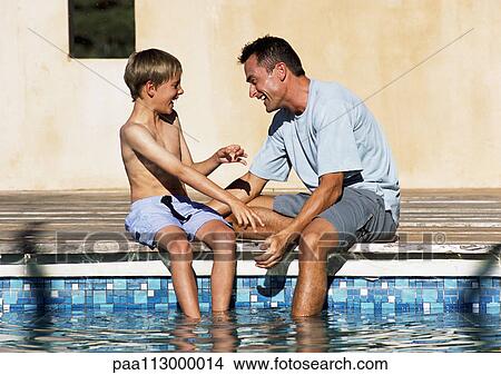 Man and young boy sitting together, feet in pool. View Large Photo Image Picture - Man and young boy sitting together, feet in pool.. Fotosearch