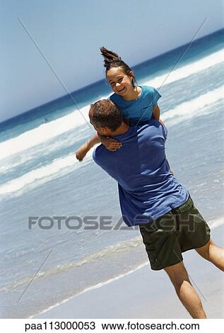 Stock Image - Man carrying young girl on the beach.. Fotosearch