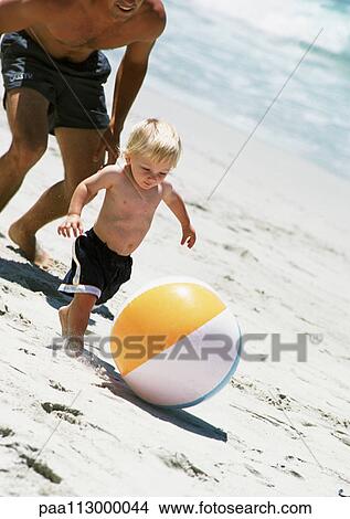 Man following child kicking ball at the beach. View Large Photo Image Picture - Man following child kicking ball at the beach.. Fotosearch