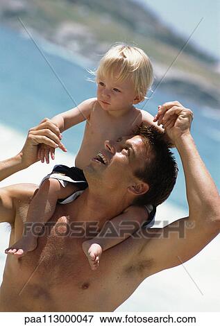 Man looking up at young child on his shoulders at the beach. View Large Photo Image Stock Photo - Man looking up at young child on his shoulders at the beach.. Fotosearch