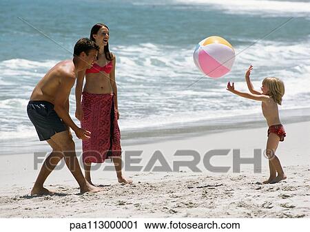 Stock Image - Young couple playing ball with child at the beach.. Fotosearch