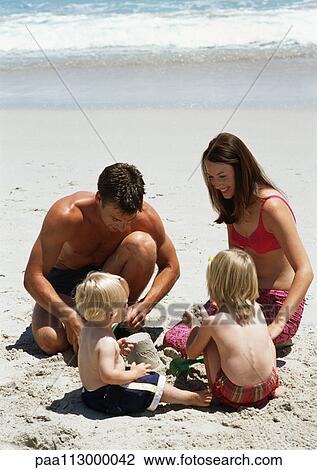Young family building a sandcastle at the beach. View Large Photo Image Stock Image - Young family building a sandcastle at the beach.. Fotosearch