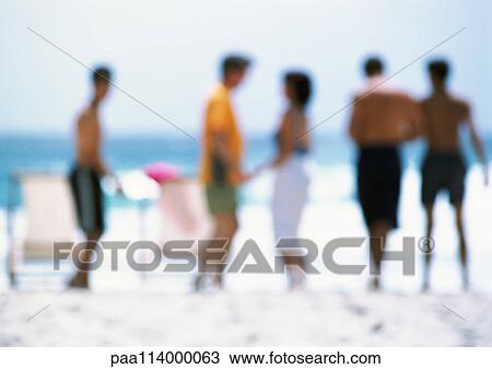 Stock Image - Adults standing on beach, blurred. Fotosearch