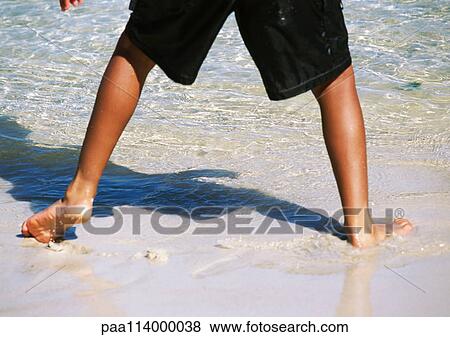 Stock Photo - Boy standing at edge of water, lower section. Fotosearch