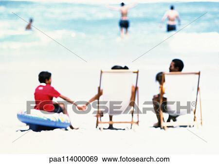 Stock Photo - Family sitting on beach, rear view. Fotosearch