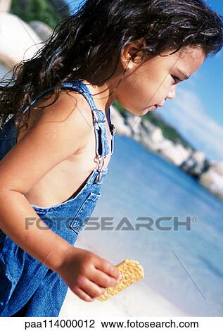 Stock Image - Little girl holding snack on beach, side view, close-up. Fotosearch