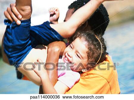 Stock Photograph - Man holding daughter on his shoulder with legs in the air, girl laughing. Fotosearch