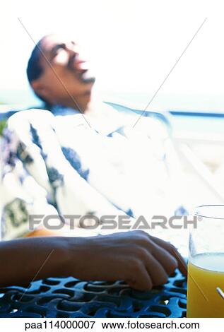 Person's hand on table next to glass of juice, second person sleeping in background View Large Photo Image Stock Photo - Person's hand on table next to glass of juice, second person sleeping in background. Fotosearch