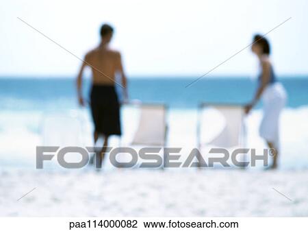 Stock Image - Two adults standing next to chairs on beach, blurred. Fotosearch