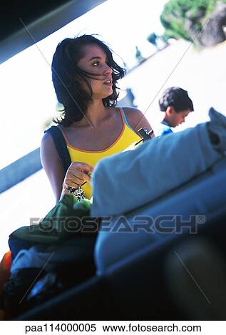 Stock Photography - Woman standing behind car trunk holding beach things. Fotosearch