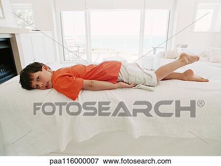 Stock Photo - Boy on bed lying on stomach. Fotosearch