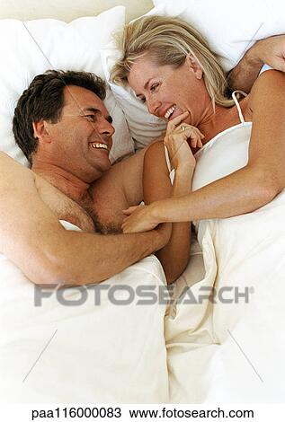 Couple lying in bed smiling and laughing View Large Photo Image Stock Image - Couple lying in bed smiling and laughing. Fotosearch