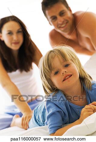 Stock Photo - Girl on bed, parents in background. Fotosearch
