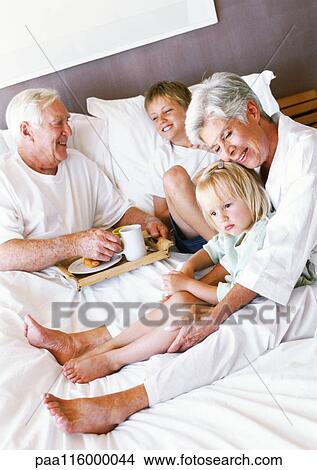 Grandparents and children sitting on bed View Large Photo Image Picture - Grandparents and children sitting on bed. Fotosearch