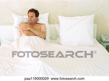 Stock Photo - Man lying in bed, arms folded over chest. Fotosearch