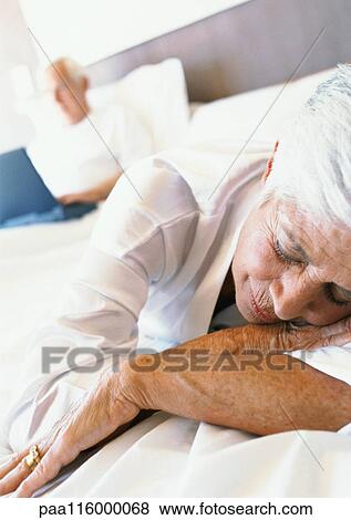Mature woman sleeping, man using laptop in bed in background View Large Photo Image Stock Photo - Mature woman sleeping, man using laptop in bed in background. Fotosearch