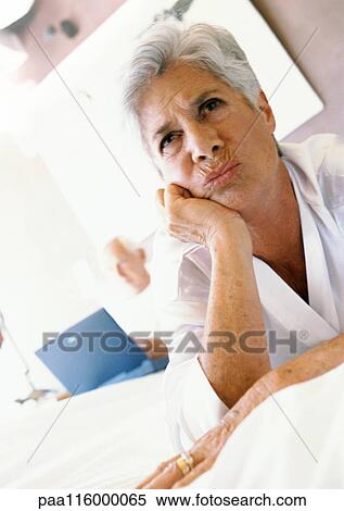 Stock Photography - Mature woman with hand under chin, man using laptop in background. Fotosearch
