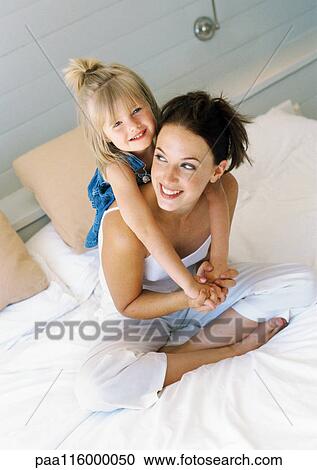 Mother sitting on bed, holding girl on back View Large Photo Image Stock Image - Mother sitting on bed, holding girl on back. Fotosearch