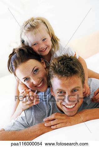 Picture - Parents and daughter lying piled on top of each other. Fotosearch