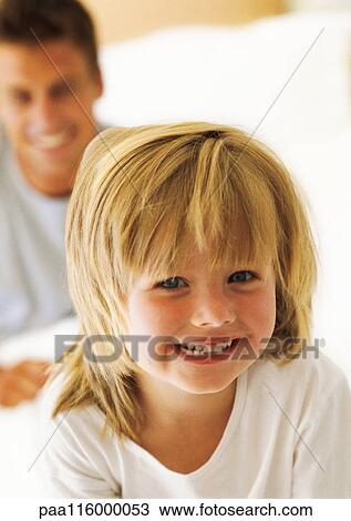 Stock Image - Small girl smiling, father in background, portrait. Fotosearch