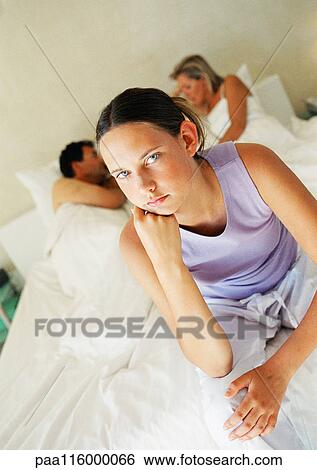Teenage girl sitting on parent's bed, parents lying in background View Large Photo Image Stock Photograph - Teenage girl sitting on parent's bed, parents lying in background. Fotosearch