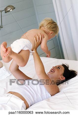 Woman lying on bed holding up baby in air View Large Photo Image Stock Image - Woman lying on bed holding up baby in air. Fotosearch
