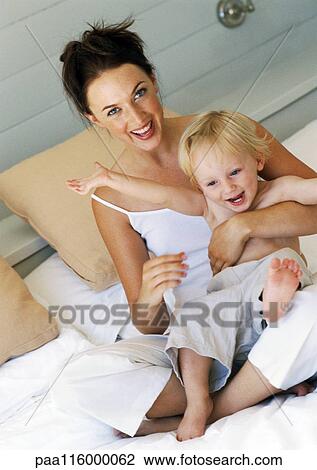 Woman on bed holding baby, smiling View Large Photo Image Stock Image - Woman on bed holding baby, smiling. Fotosearch