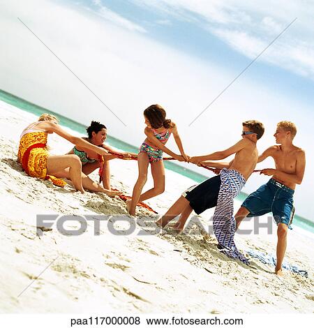 Stock Photo - Group of people playing tug of war on the beach. Fotosearch