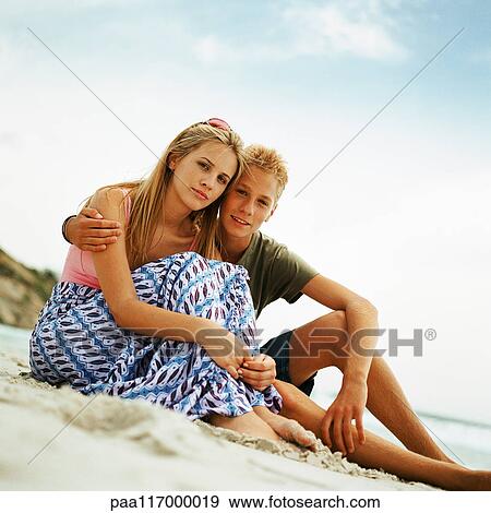 Teenage boy and girl sitting side by side on sand at the beach View Large Photo Image Stock Photo - Teenage boy and girl sitting side by side on sand at the beach. Fotosearch