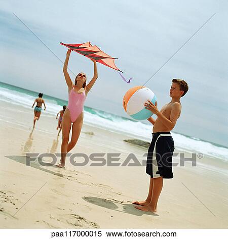 Teenage boy holding beach ball, girl holding kite at the beach View Large Photo Image Stock Photography - Teenage boy holding beach ball, girl holding kite at the beach. Fotosearch