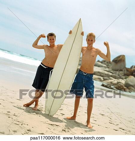 Stock Photograph - Two boys on beach holding surfboard. Fotosearch