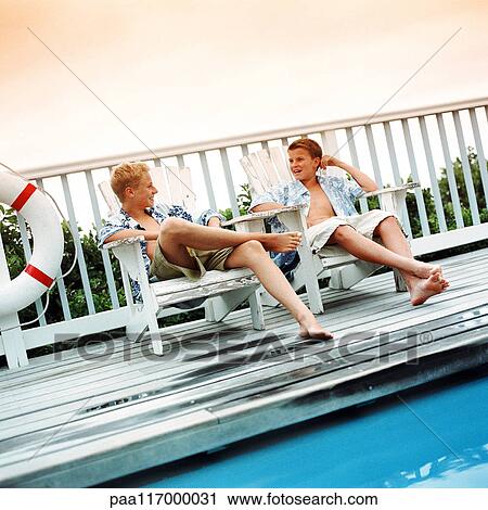 Two boys sitting in lounge chairs on side of swimming pool View Large Photo Image Stock Image - Two boys sitting in lounge chairs on side of swimming pool. Fotosearch